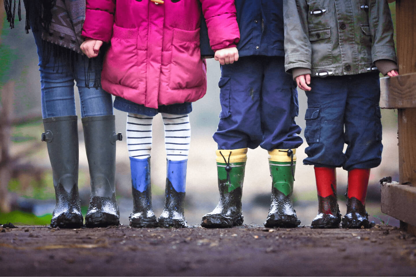 A row of children standing outdoors in coats and wellington boots