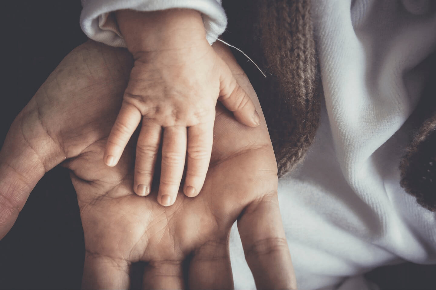 An adult's hand resting gently on a baby's back