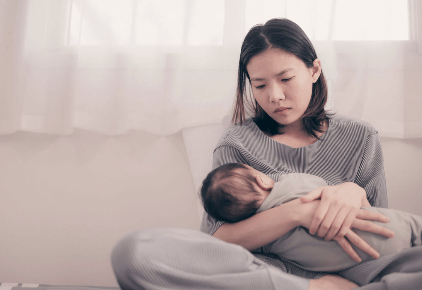 A young mother sitting on a sofa holding her newborn baby