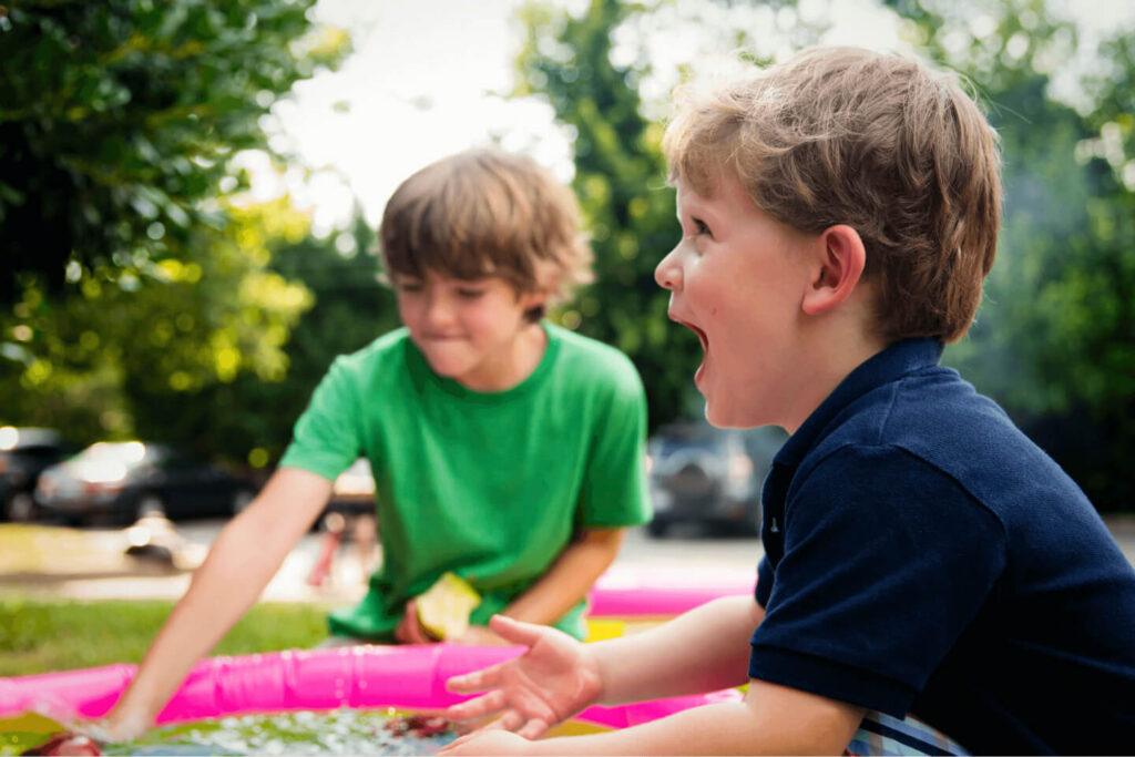 Two young boys sitting outdoors on a mat, laughing together
