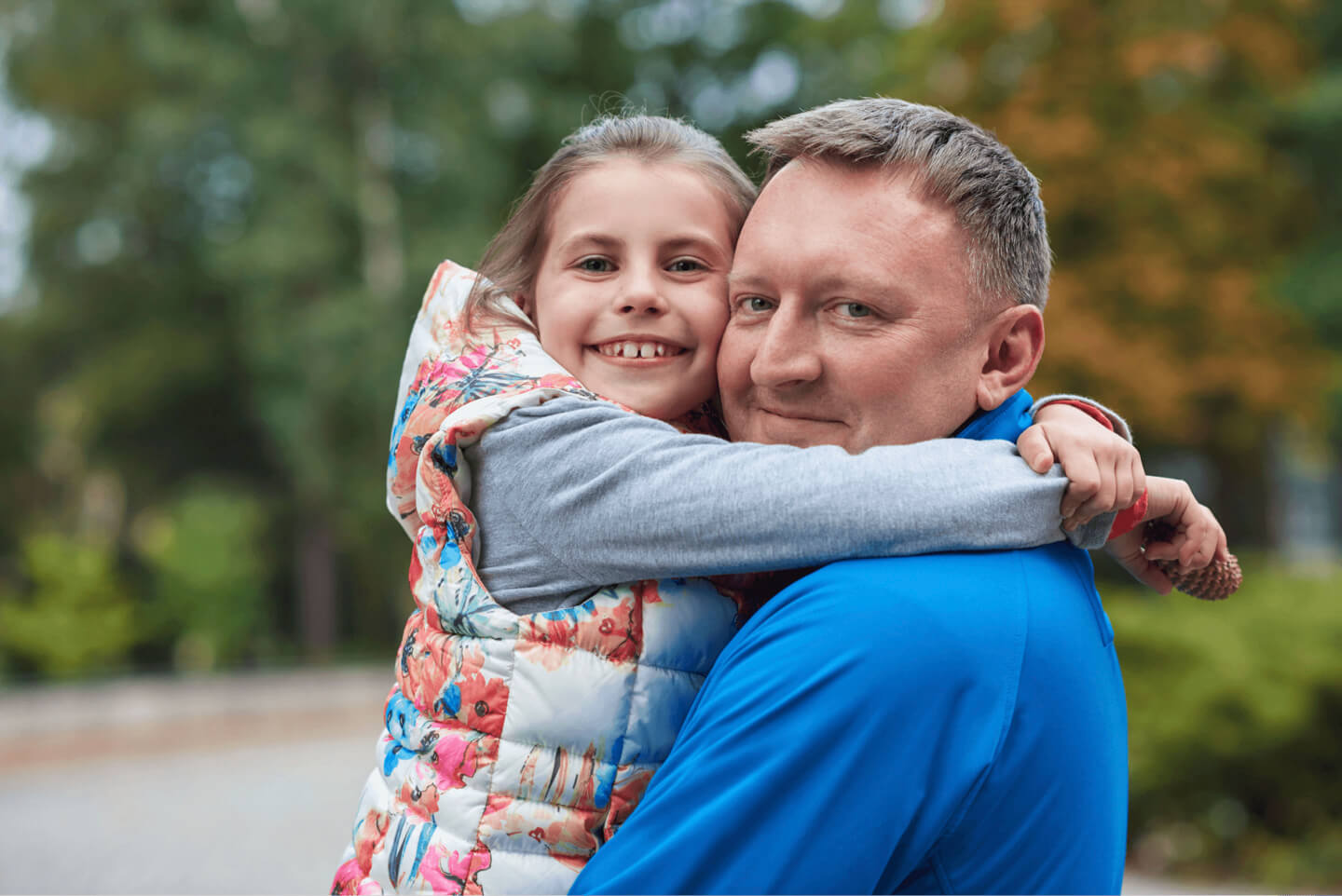 An older man hugging his granddaughter outdoors in autumn