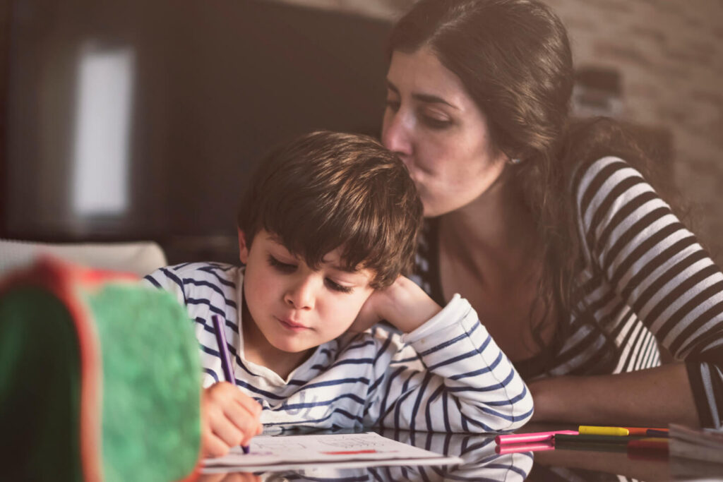 A woman helping a young boy with his schoolwork at a table