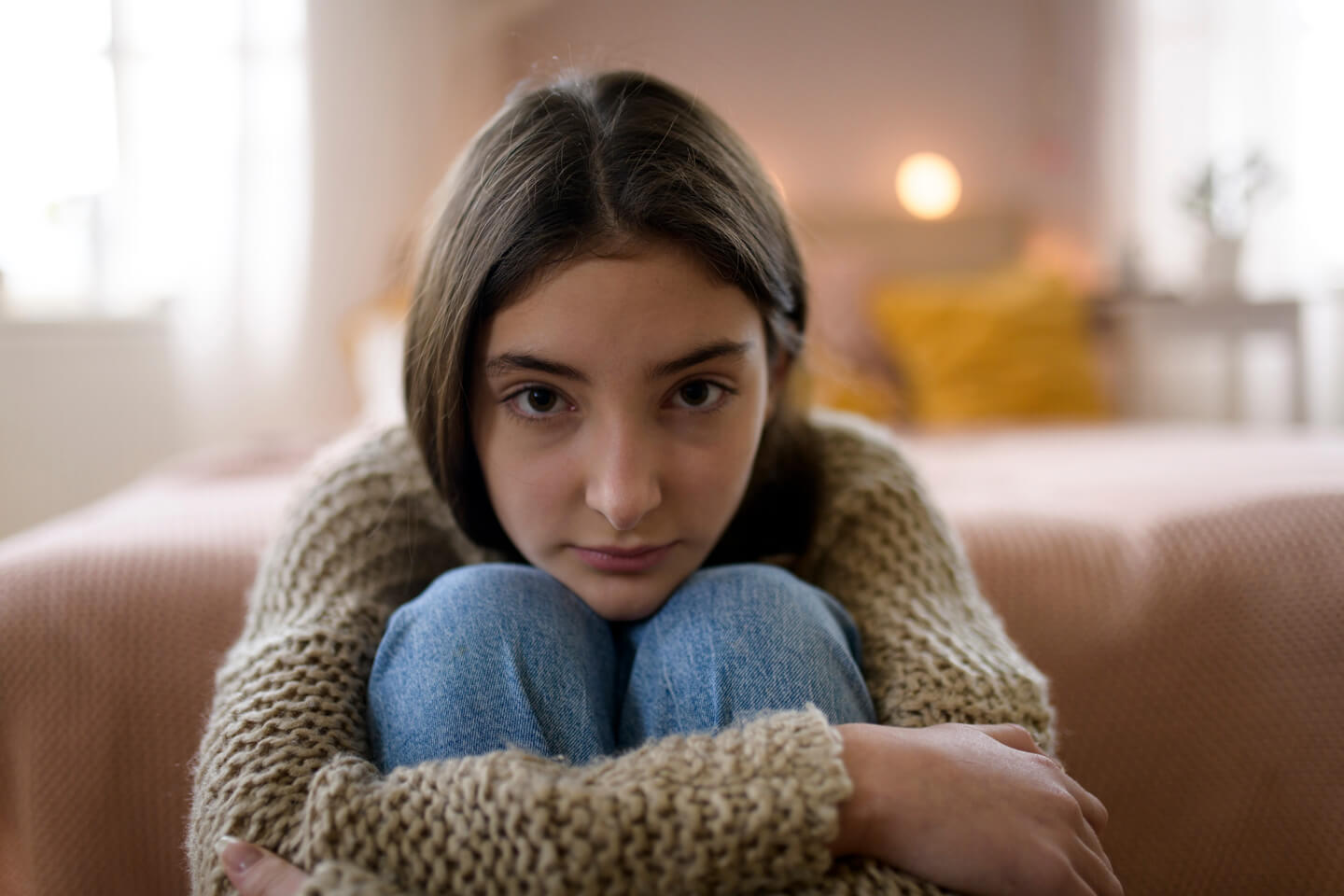 A teenage girl sitting on a sofa with her knees drawn up