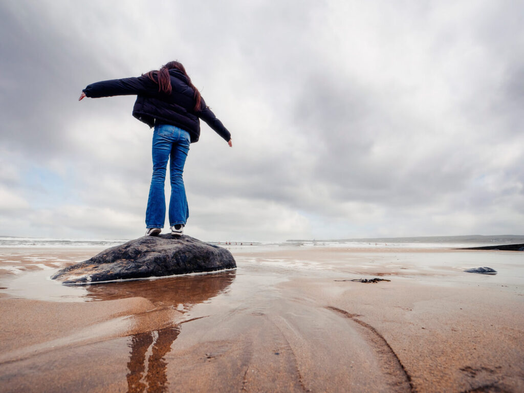A person standing on a rock at the shoreline with arms outstretched
