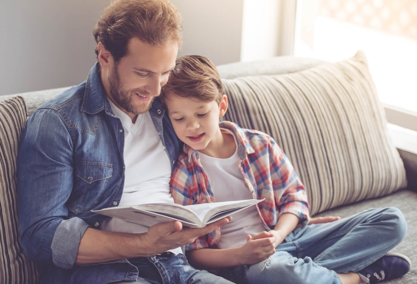 A father and son reading a book together on a sofa
