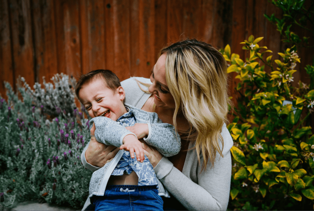 A mother laughing with her toddler in a garden